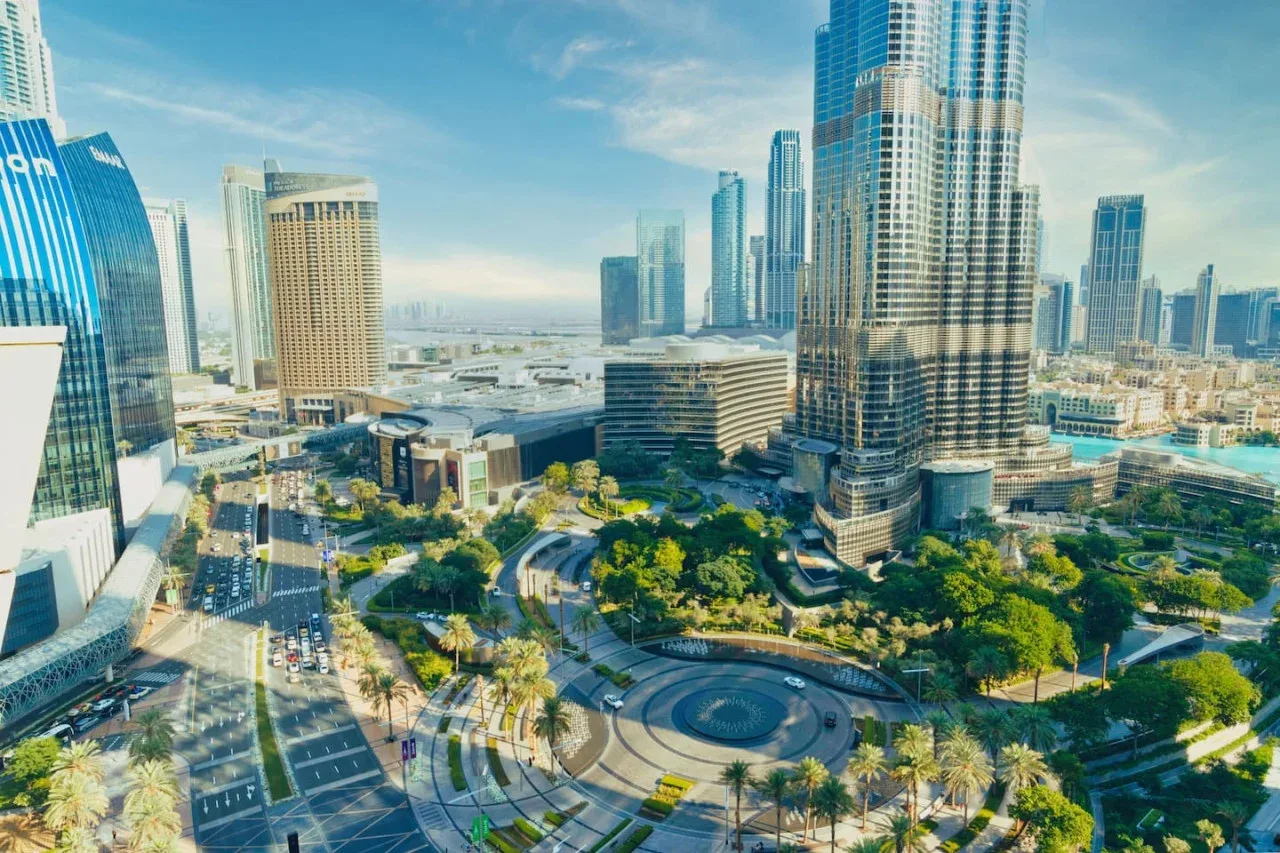 Vista aérea del centro de una ciudad con edificios altos, calles y una plaza ajardinada.