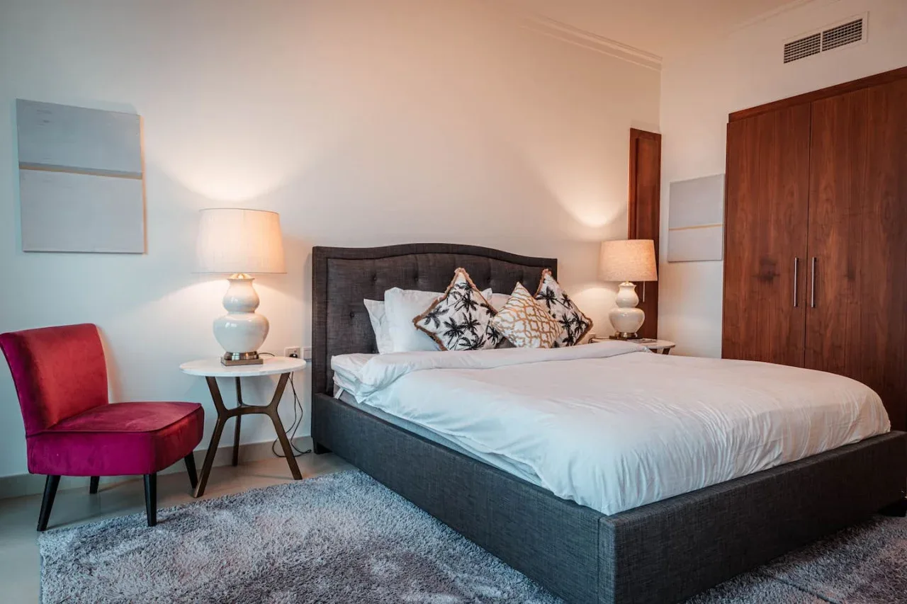 Un dormitorio con una cama grande, mesitas de noche y una silla tapizada roja.