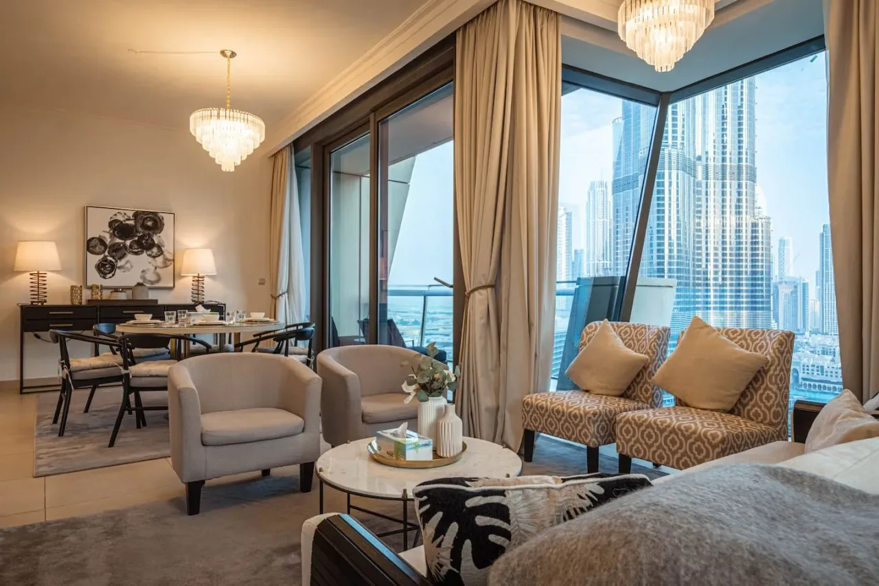 Sala de estar y comedor con asientos junto a grandes ventanales con vistas a edificios de la ciudad.