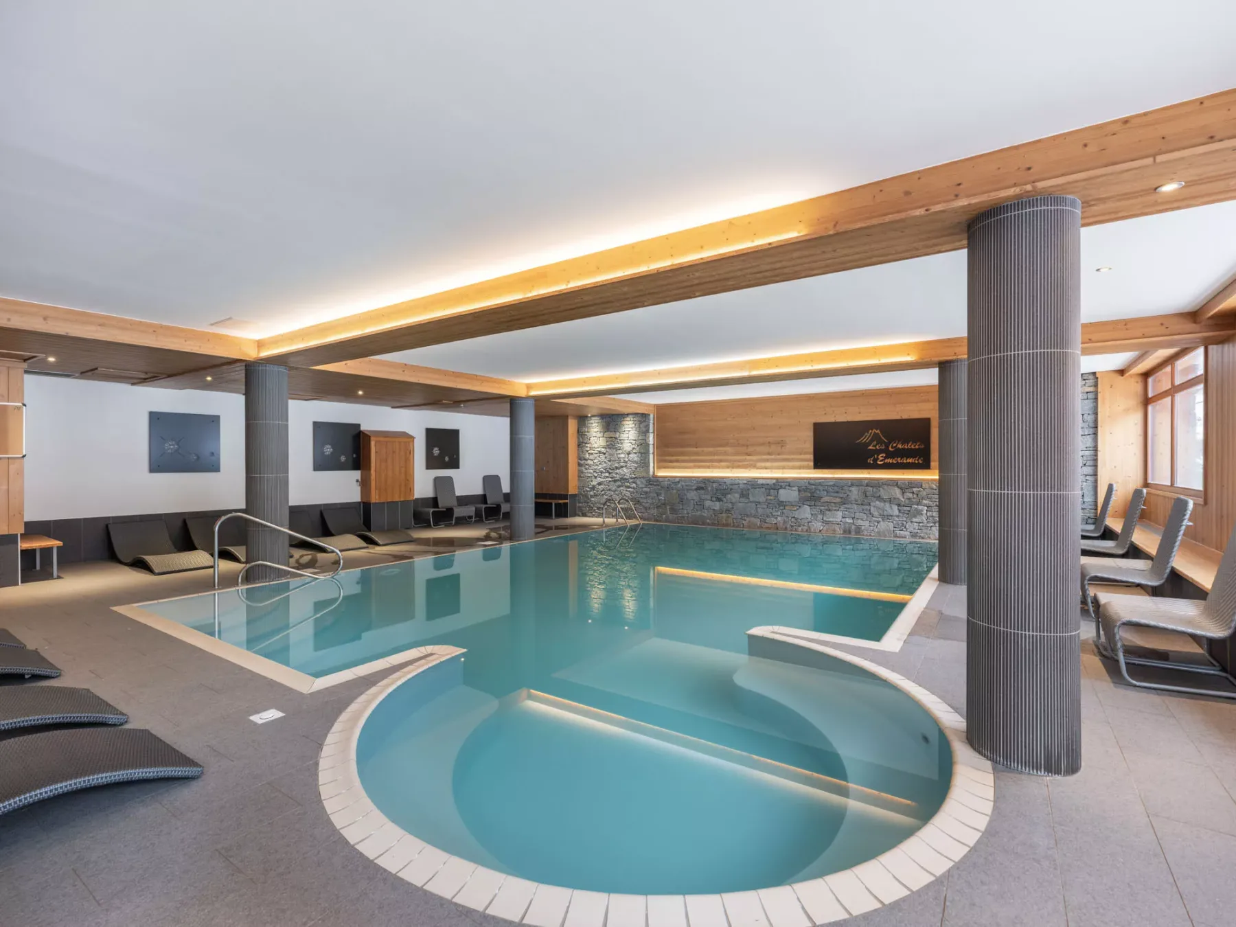 Una piscina cubierta con una zona poco profunda redondeada y asientos junto a las ventanas.