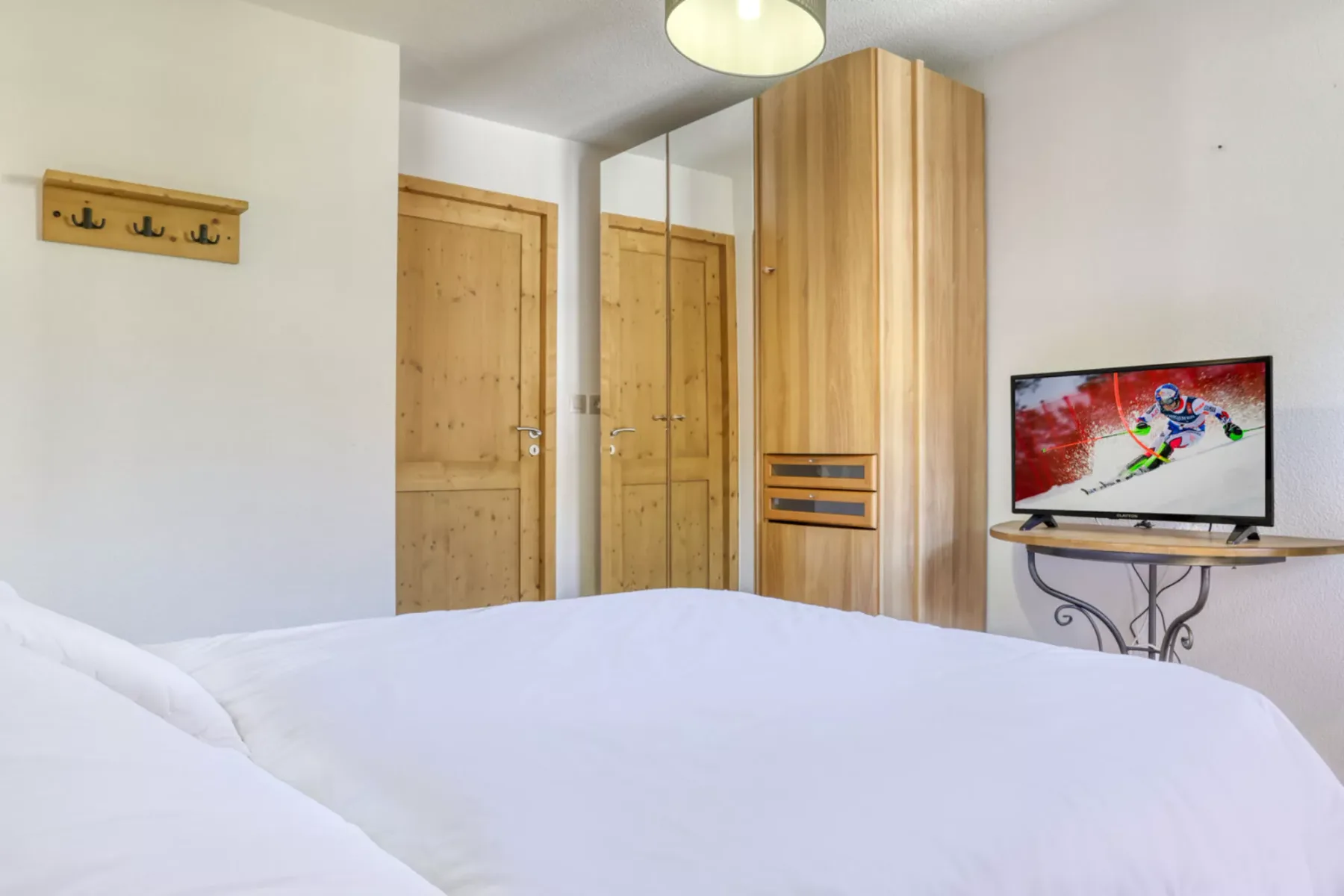 Un dormitorio con una cama blanca, puertas de madera y un televisor.