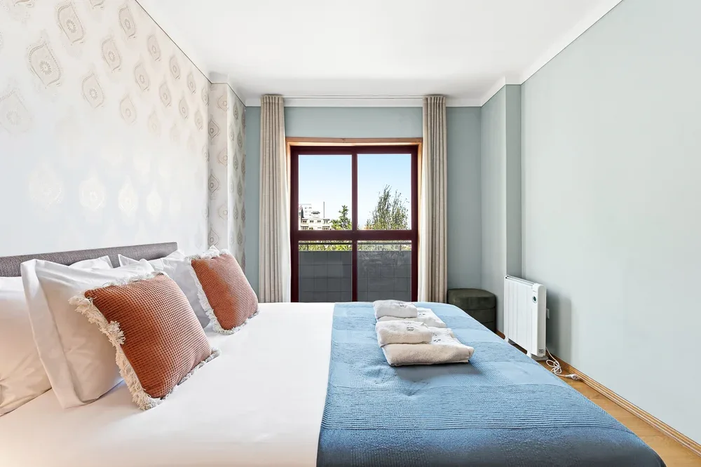 A bedroom with a bed dressed in white and blue linens beside a large window.