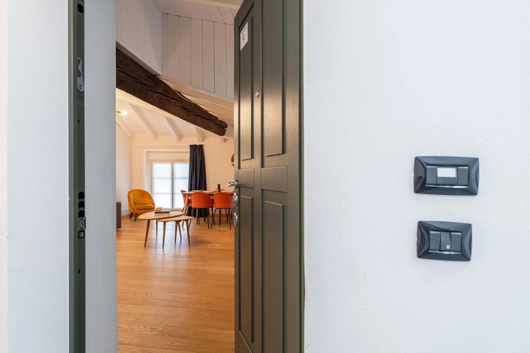 Una puerta abierta deja ver una luminosa sala de estar y comedor con suelo de madera.