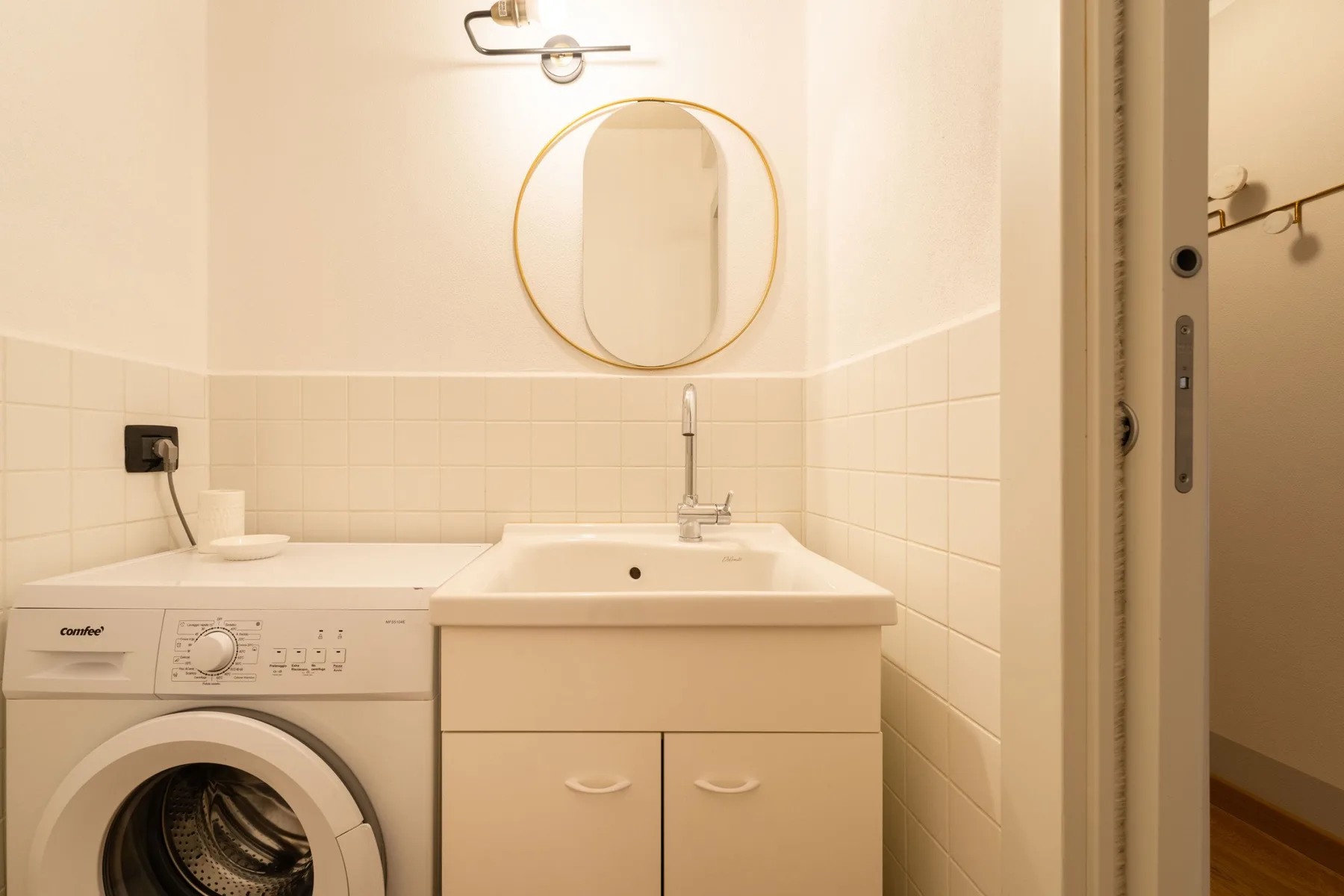 Un baño luminoso con lavabo, lavadora y espejo redondo.