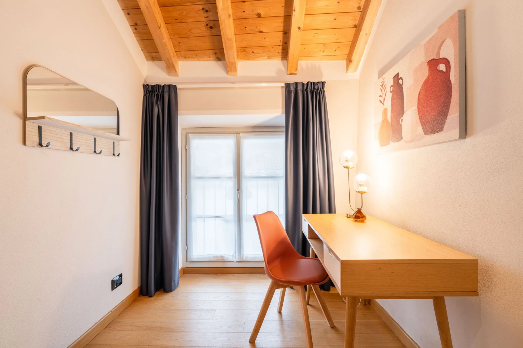 Una luminosa zona de escritorio con mesa de madera, silla y ventana bajo un techo de madera.