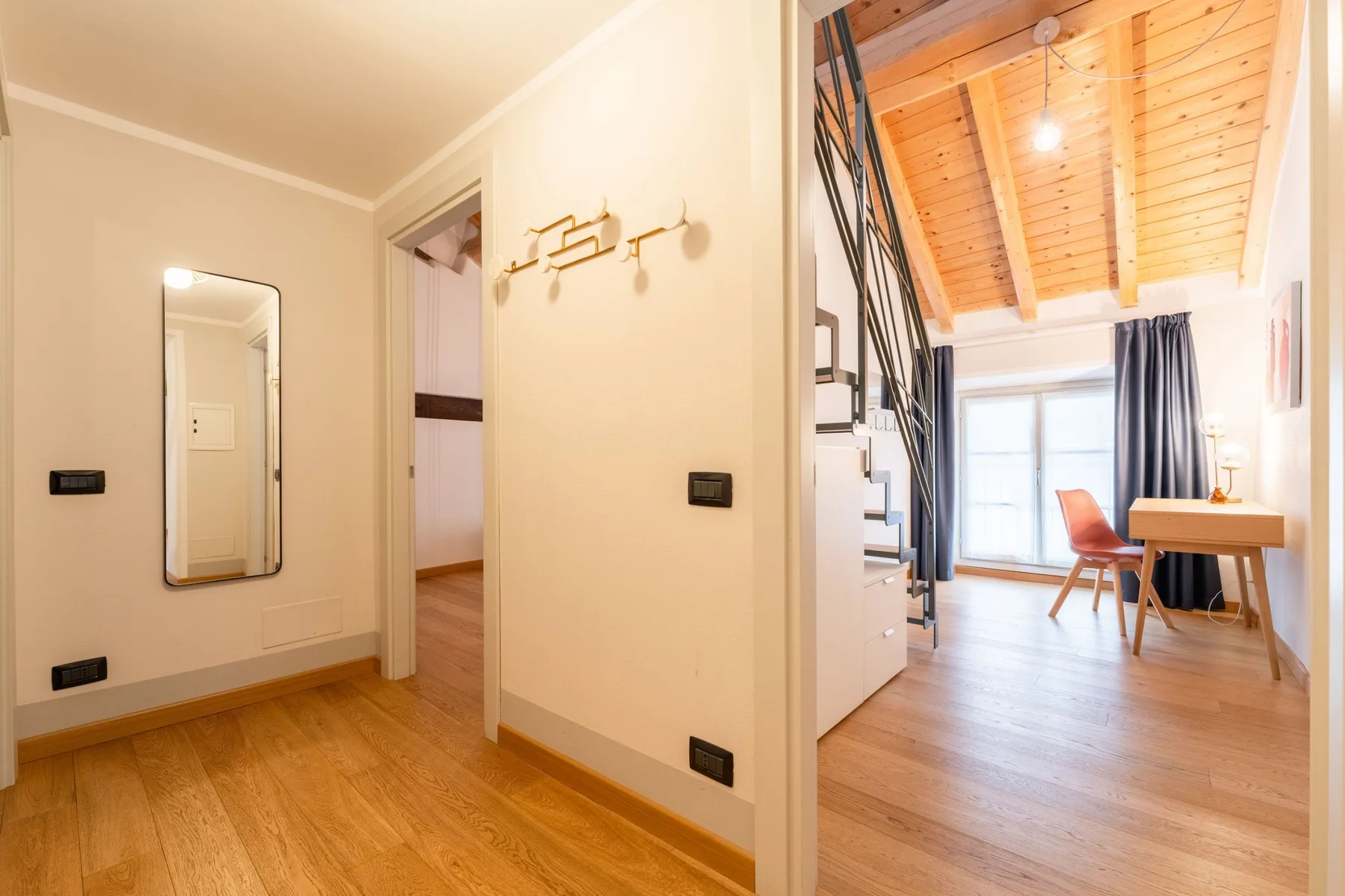 Un pasillo luminoso da a una habitación tipo loft con un escritorio junto a la ventana.