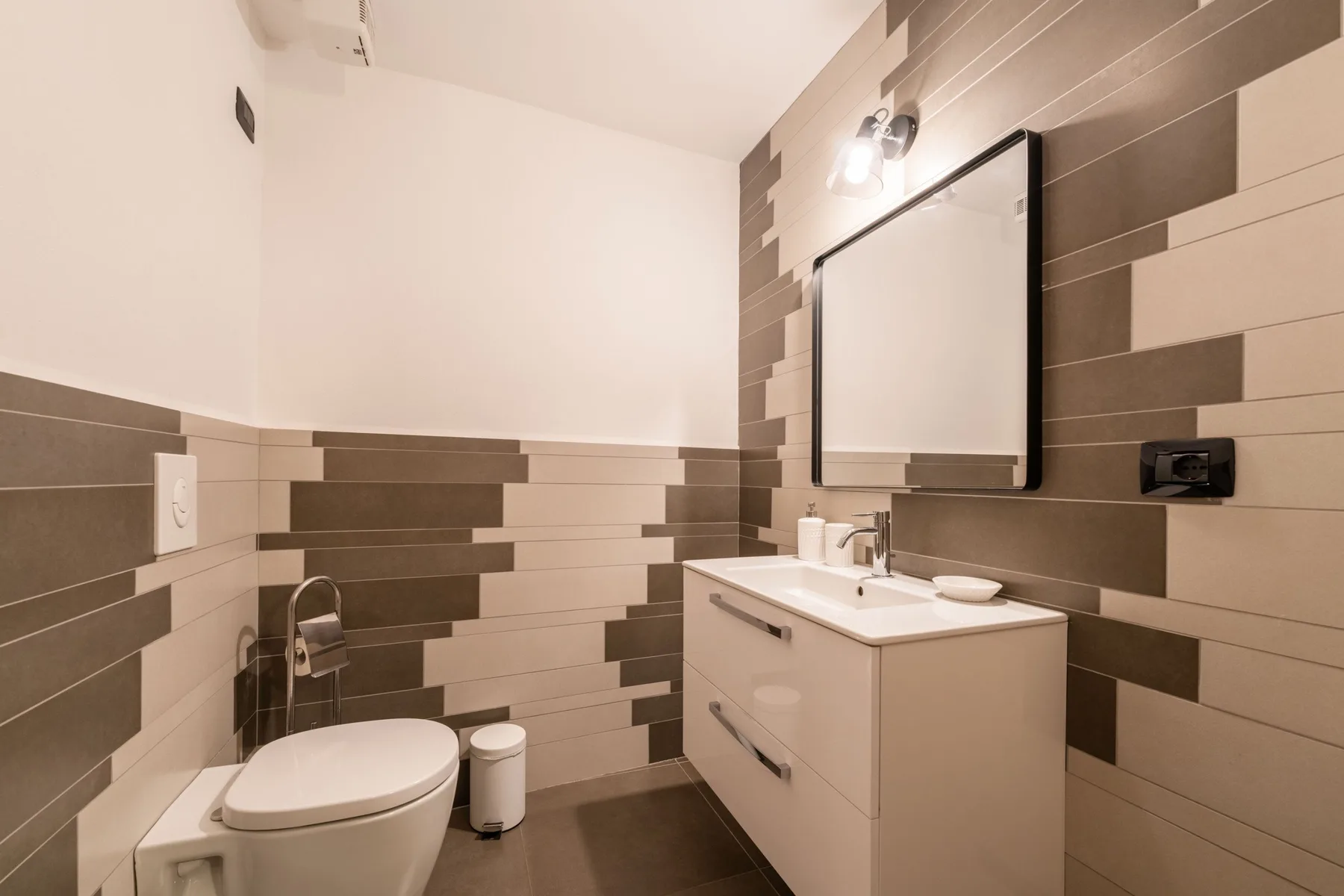 Un baño con inodoro, lavabo con mueble y un espejo grande.
