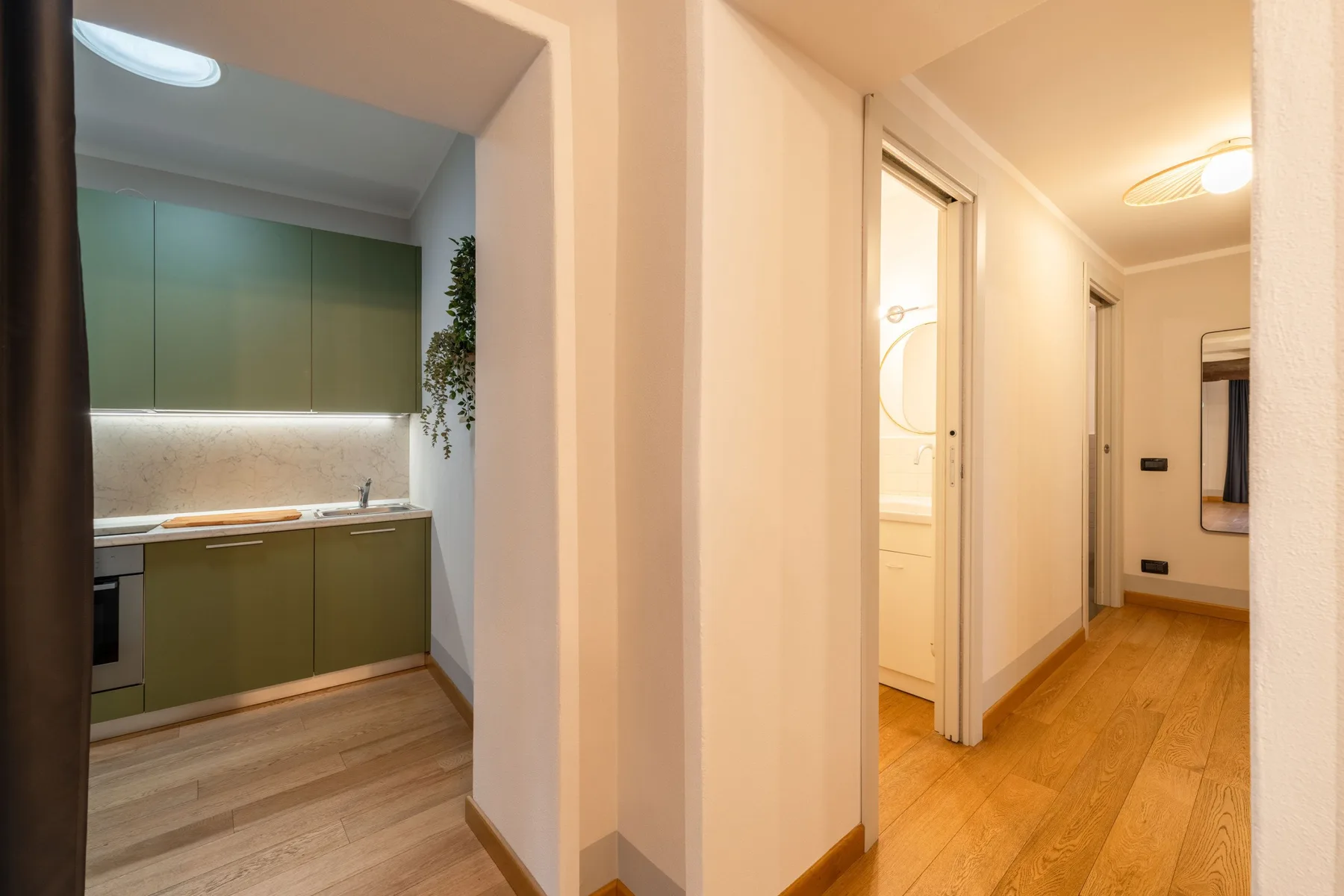 Un pasillo interior se abre a una cocina con gabinetes verdes y suelo de madera.