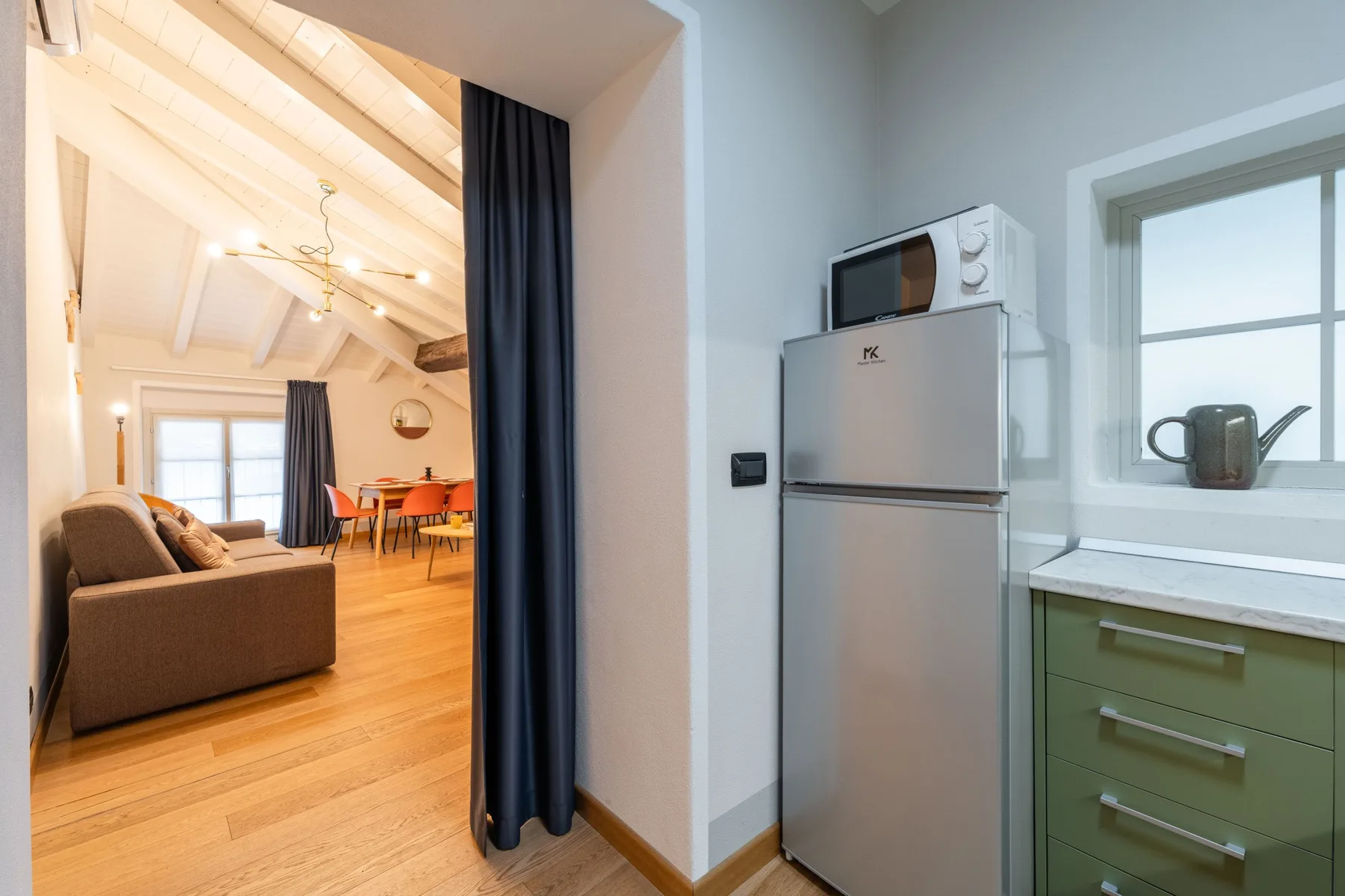 Se ve una sala con comedor junto a una pequeña cocina con refrigerador y encimera.