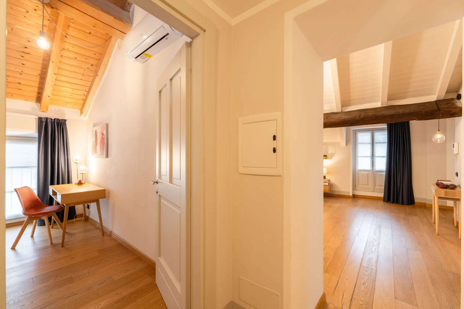 Un pasillo luminoso da a una habitación con suelo de madera y un escritorio.