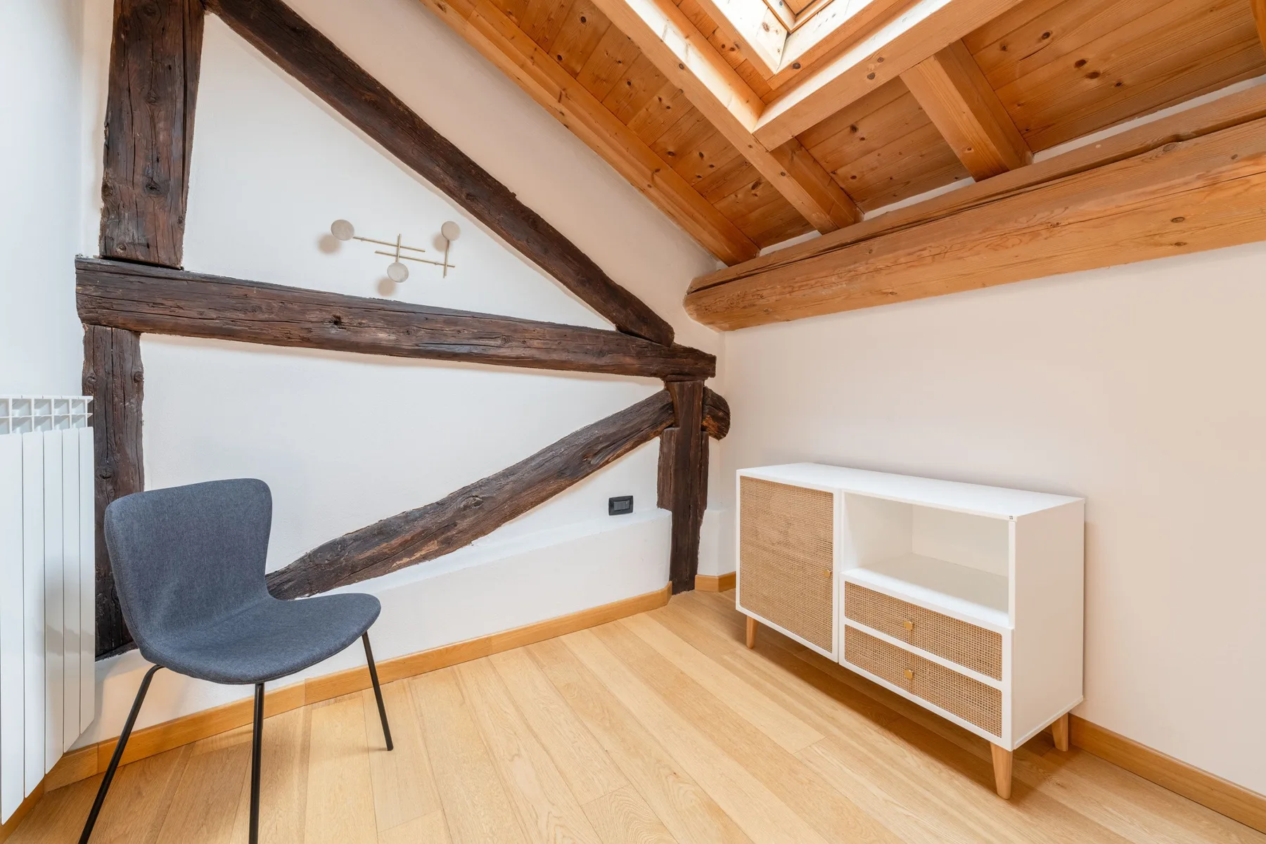 Una luminosa habitación abuhardillada con vigas de madera vistas y una claraboya.
