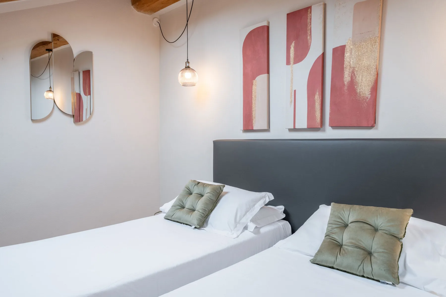 Un dormitorio con dos camas, ropa de cama clara y arte abstracto sobre un cabecero oscuro.