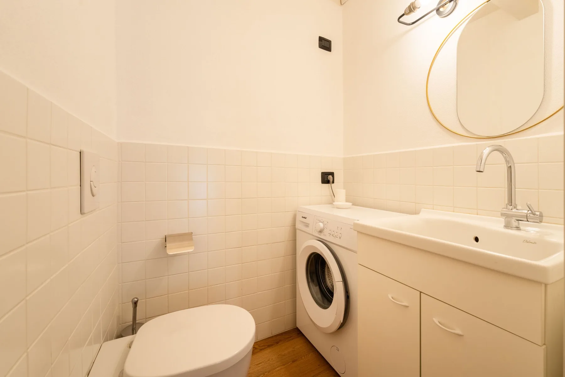 Un baño compacto con inodoro, lavadora y lavabo con mueble.