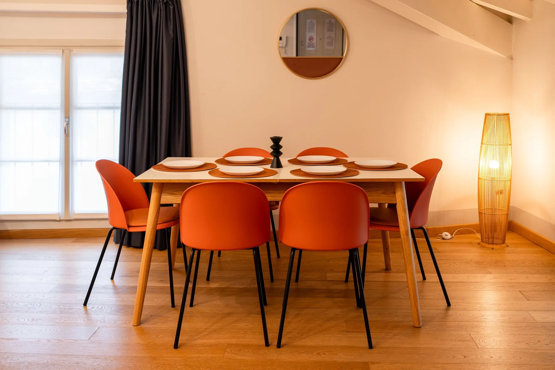 Un comedor con una mesa de madera, asientos naranjas y una lámpara de pie.