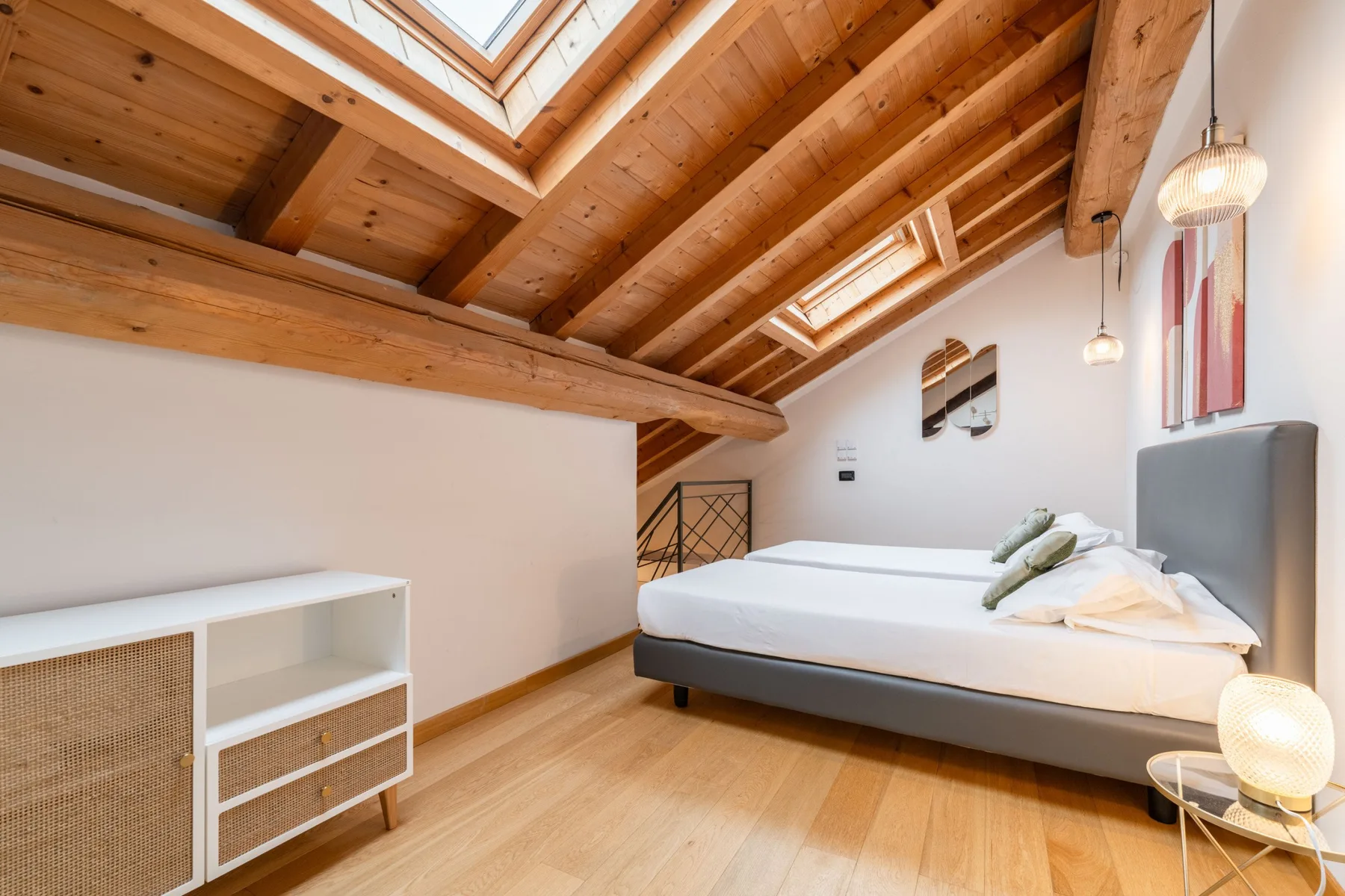 Un dormitorio con una cama bajo un techo inclinado de madera y una claraboya.