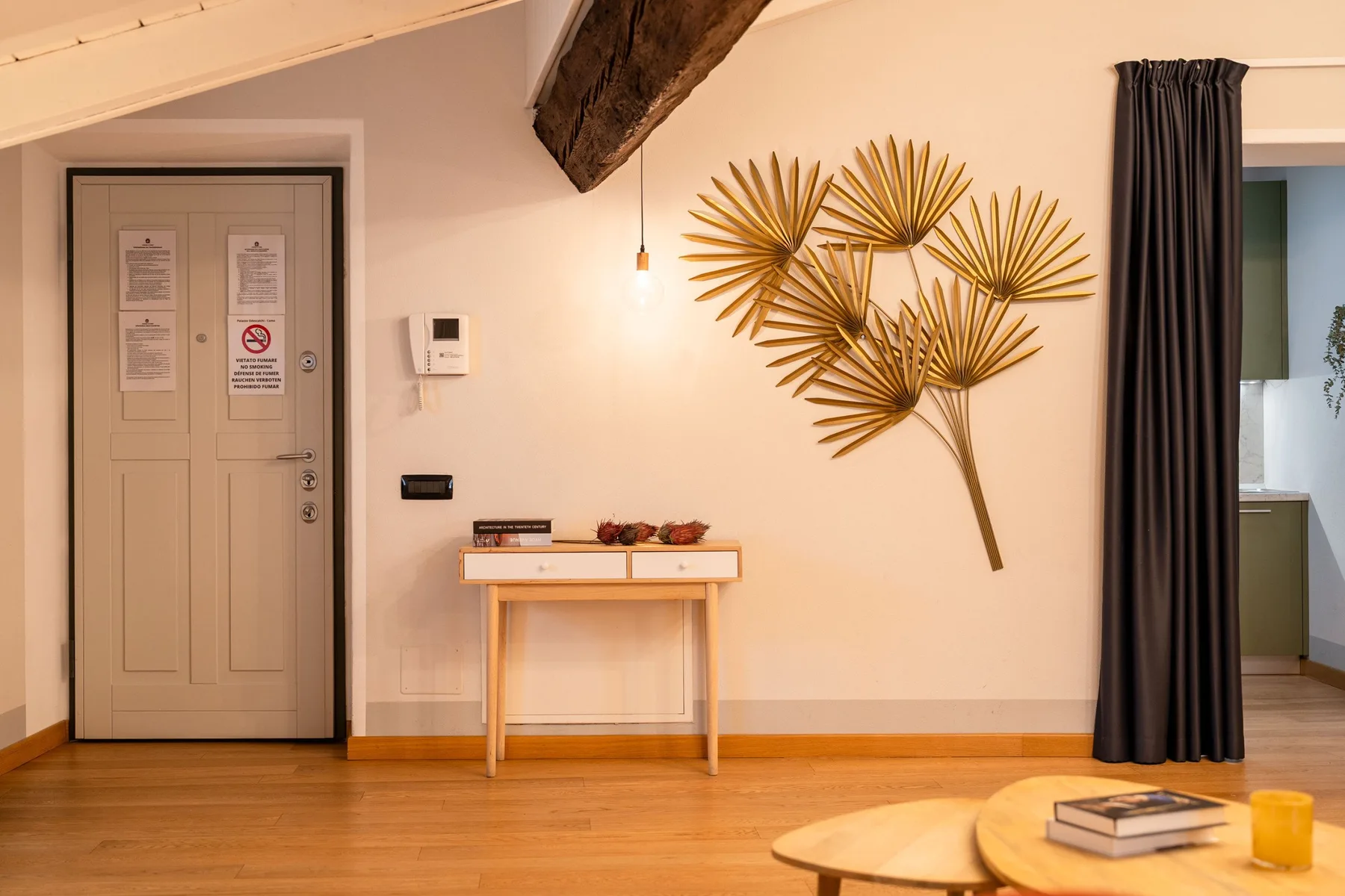 Una habitación con una puerta beige, una mesa consola y una gran decoración dorada de pared.