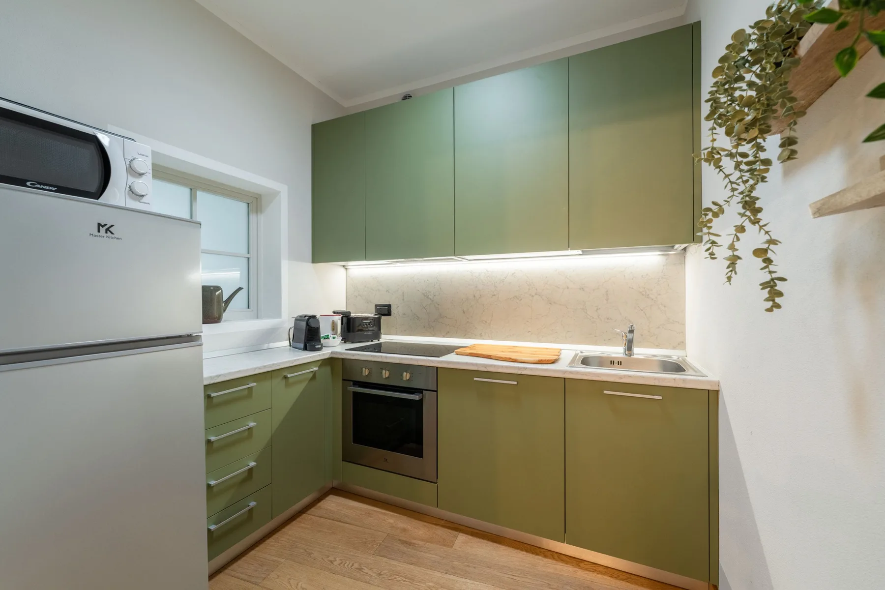 Una cocina compacta con gabinetes verdes, refrigerador y horno empotrado.