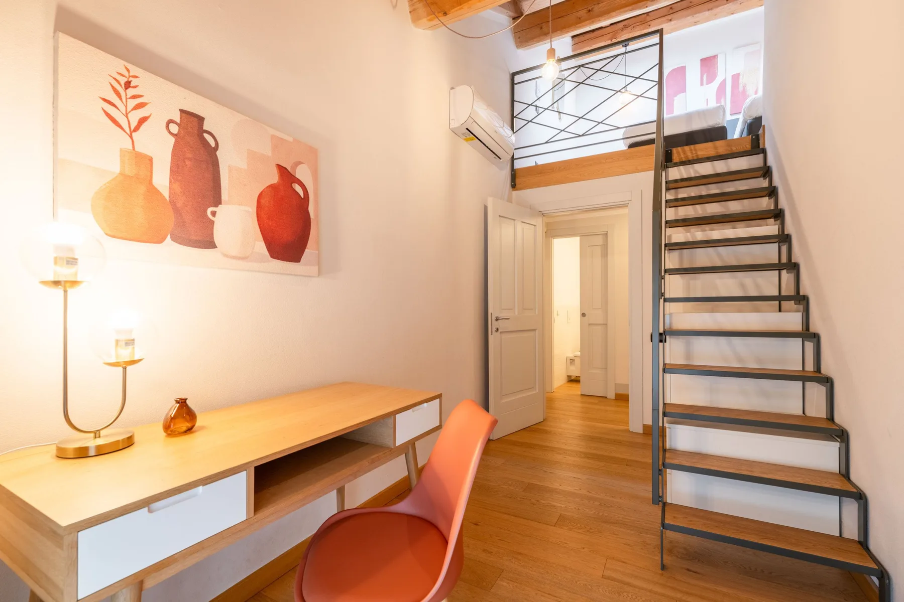 Una habitación luminosa con escritorio, arte en la pared y escaleras hacia un altillo.