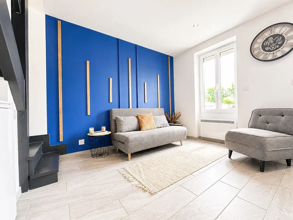 A bright living room has gray seating, a pale rug, and a bold blue accent wall.