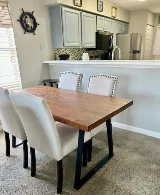 A dining area with a wooden table and white chairs beside an open kitchen.