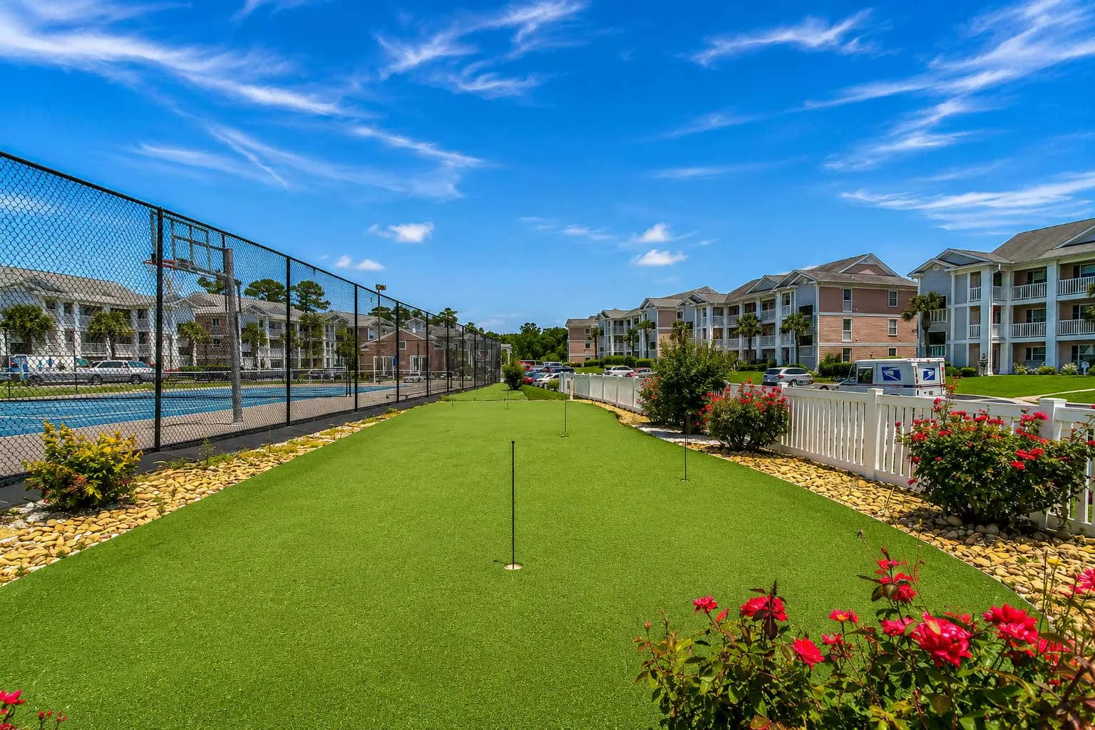 A landscaped outdoor courtyard with green lawn, flowering shrubs, and apartment buildings.