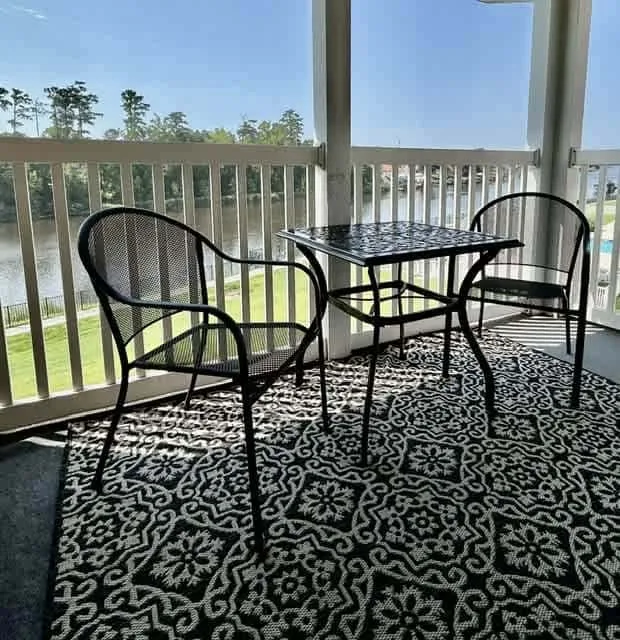 A covered balcony has black seating and a small table beside the railing.
