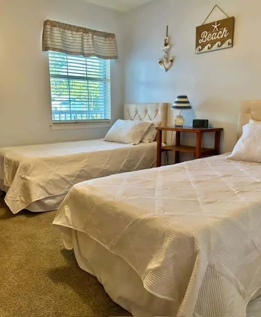 A bedroom with two beds and a window with blinds.