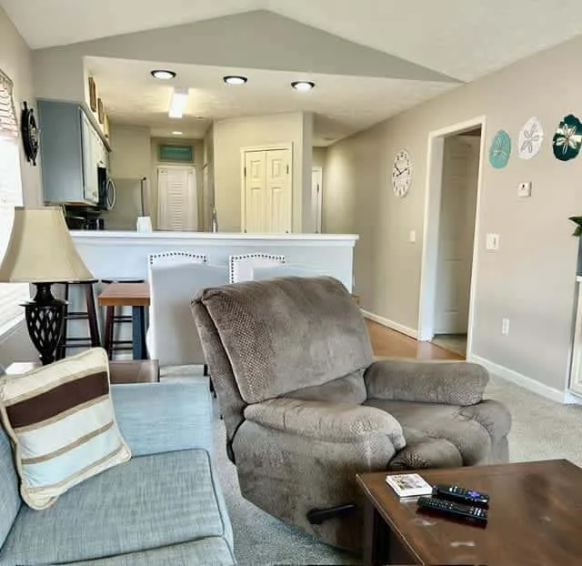 A living room with cushioned seating and a counter opening toward the kitchen.