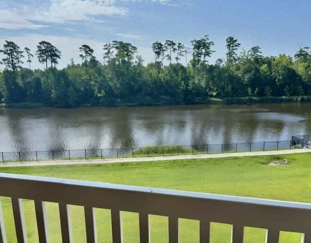 A balcony overlooks a river, with a grassy lawn and trees along the opposite bank.