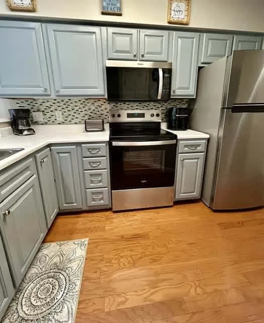 A kitchen with pale cabinets, stainless steel appliances, and wood flooring.