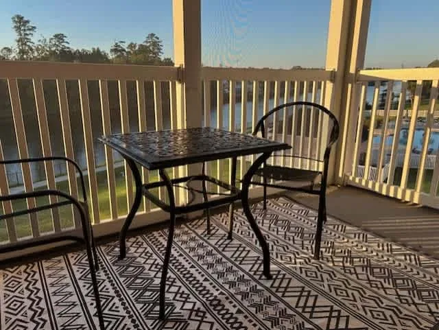 A balcony seating area with a small table and patterned rug overlooks the water.