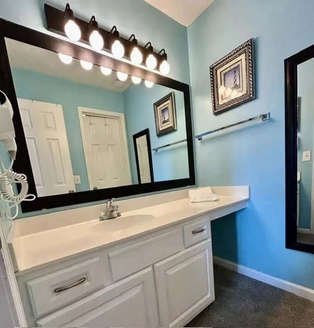A bathroom vanity with a wide mirror and wall-mounted lights.