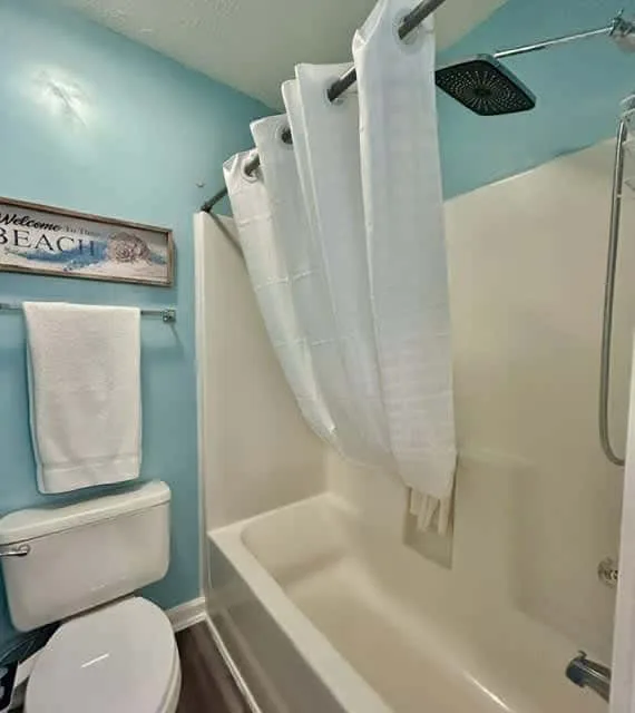 A bathroom with a bathtub, shower curtain, and towel hanging on the wall.