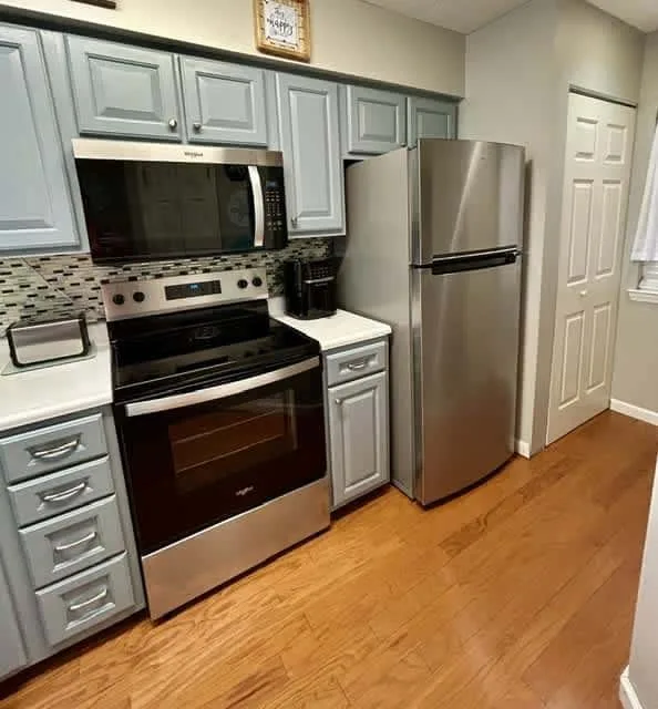 A kitchen with gray cabinetry, stainless steel appliances, and wood flooring.