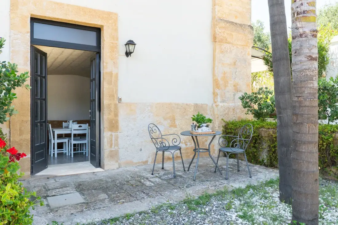A small outdoor patio with a table and chairs beside an open doorway.