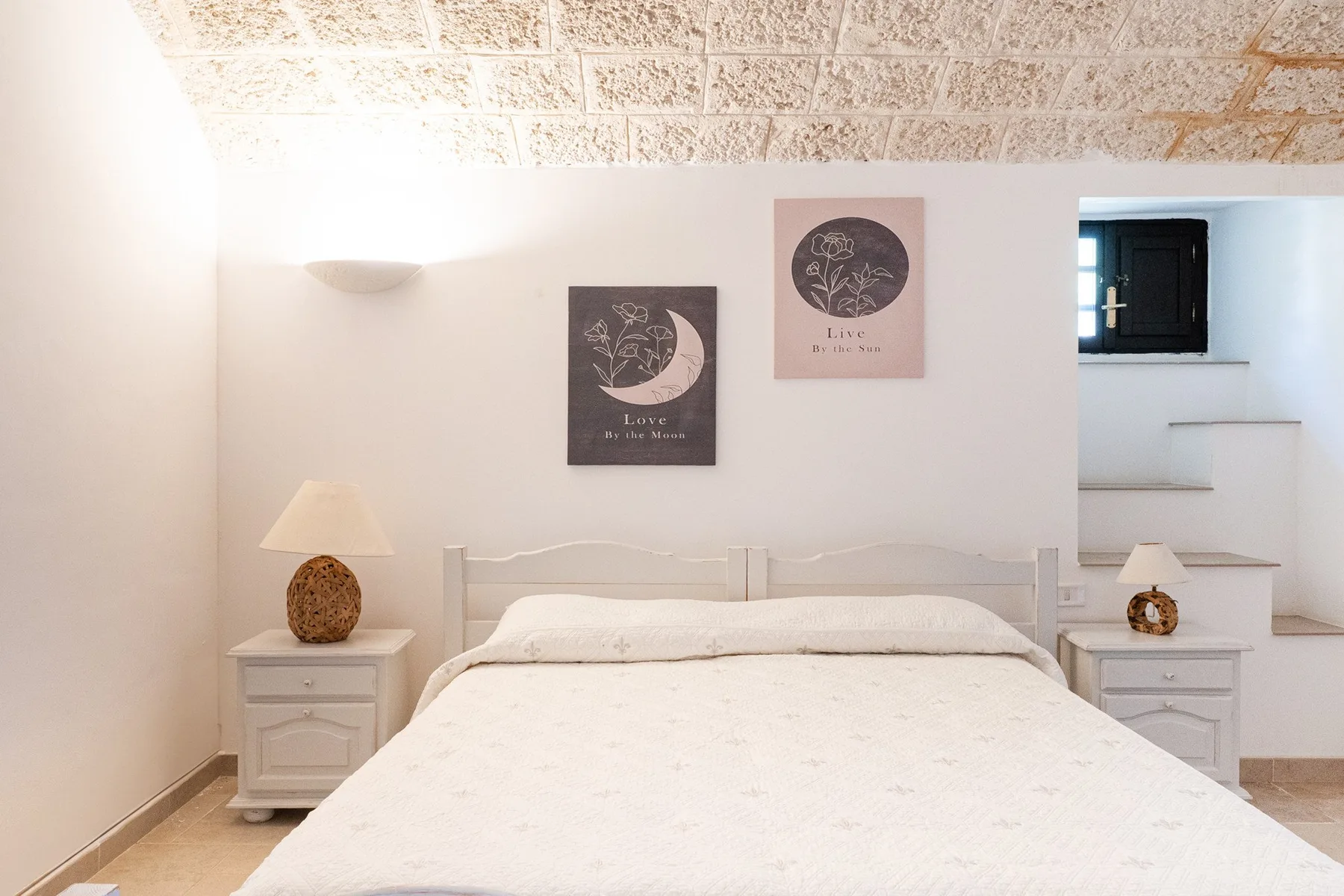 A bright bedroom with a white bed, matching bedside tables, and wall art.