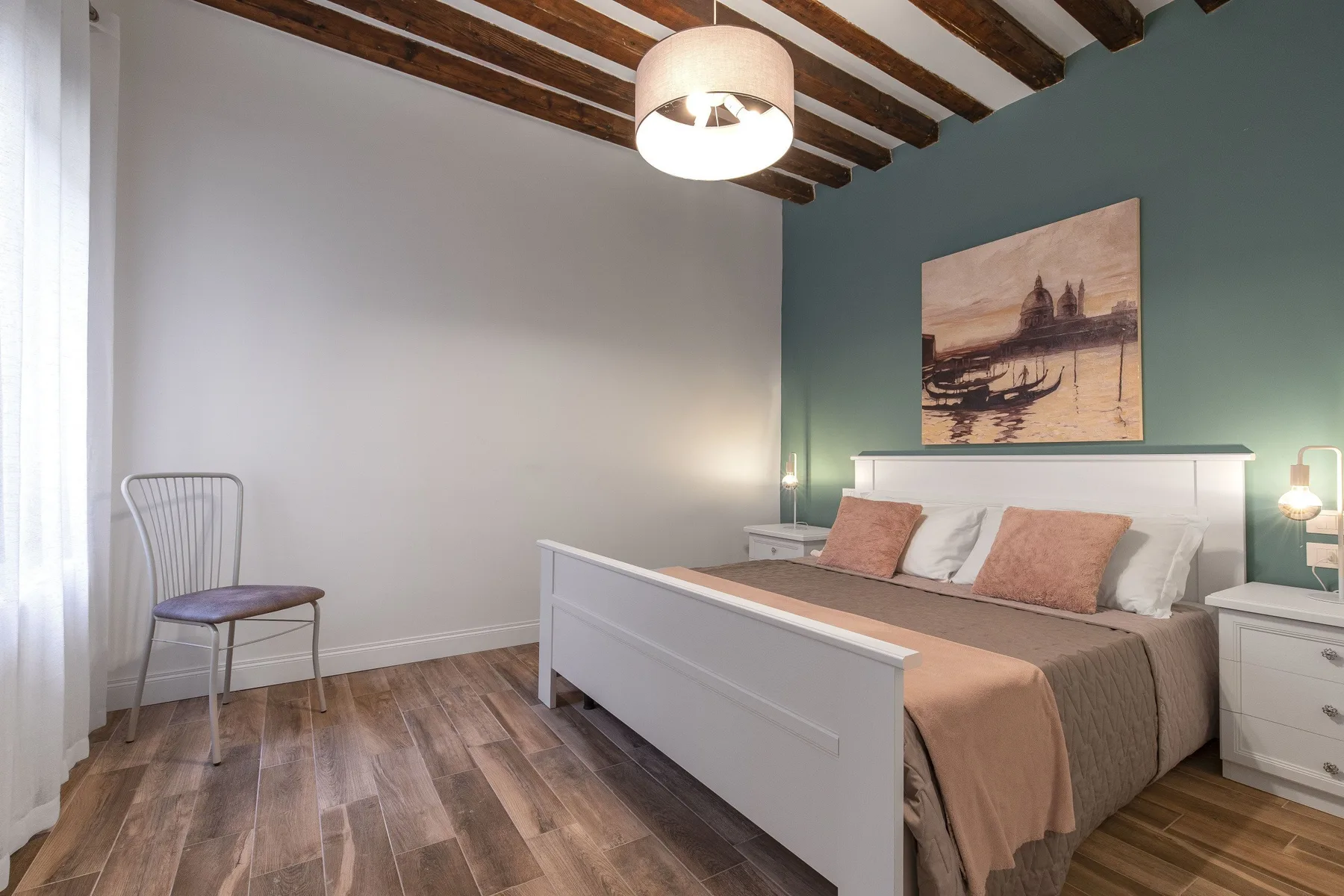 Un dormitorio con una cama junto a una pared azul y una silla cerca de la ventana.