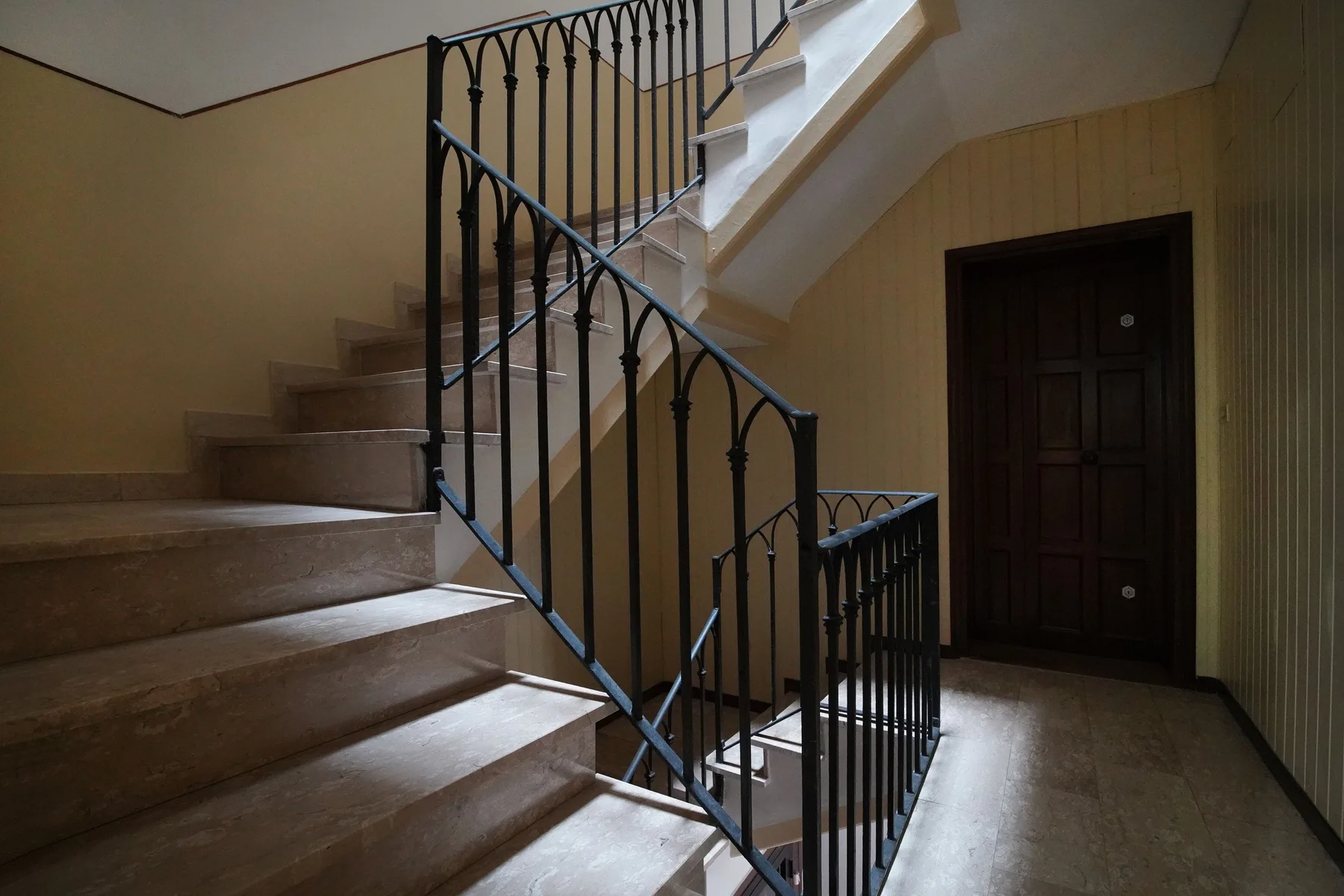 Una escalera interior con una puerta de madera oscura y barandillas negras.