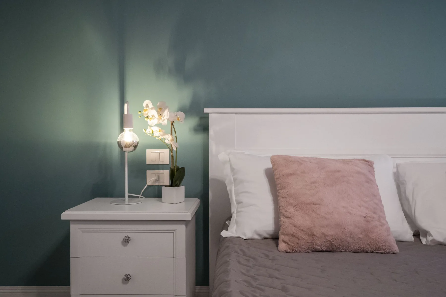 Un dormitorio con una cama, una mesita de noche y una pequeña planta en maceta.