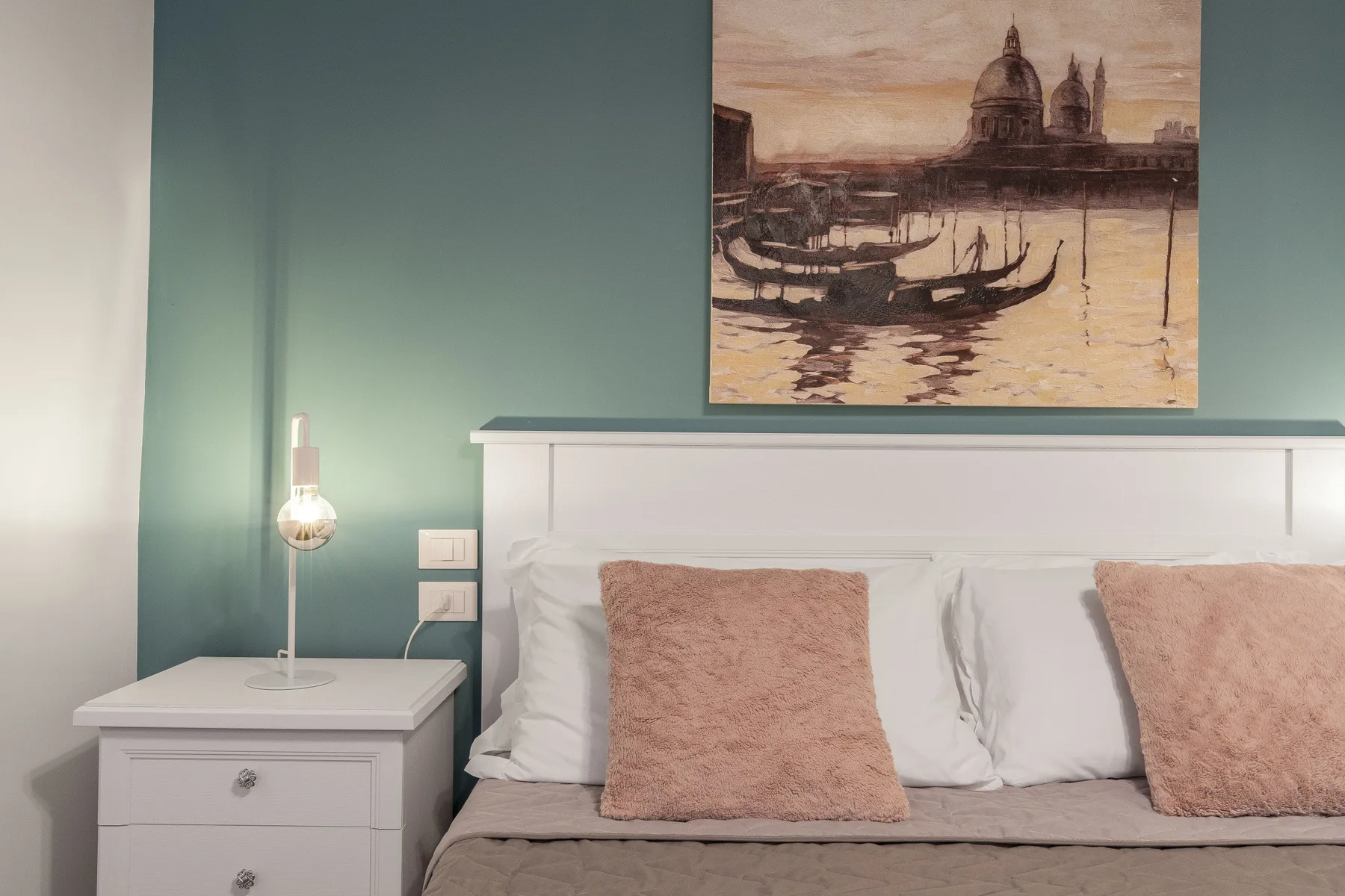 Un dormitorio con una cama blanca y una obra enmarcada sobre una pared verde azulado.