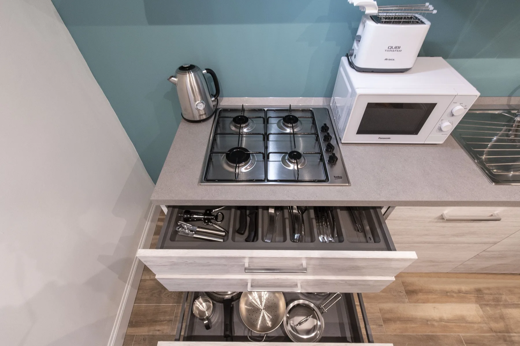 Una encimera de cocina con una placa de gas, un hervidor y un microondas.