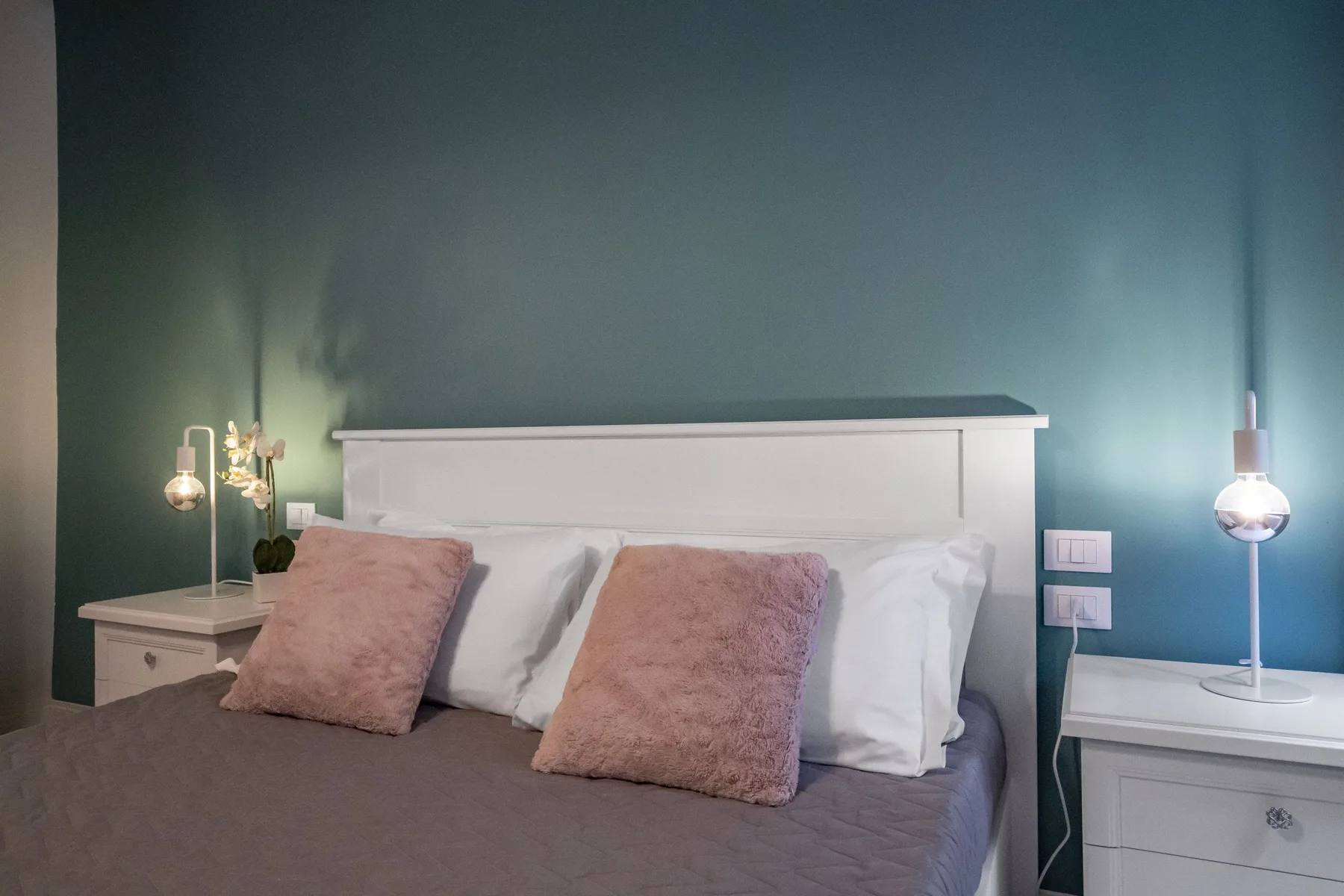 Un dormitorio con una cama vestida con ropa de cama gris y cojines rosas.
