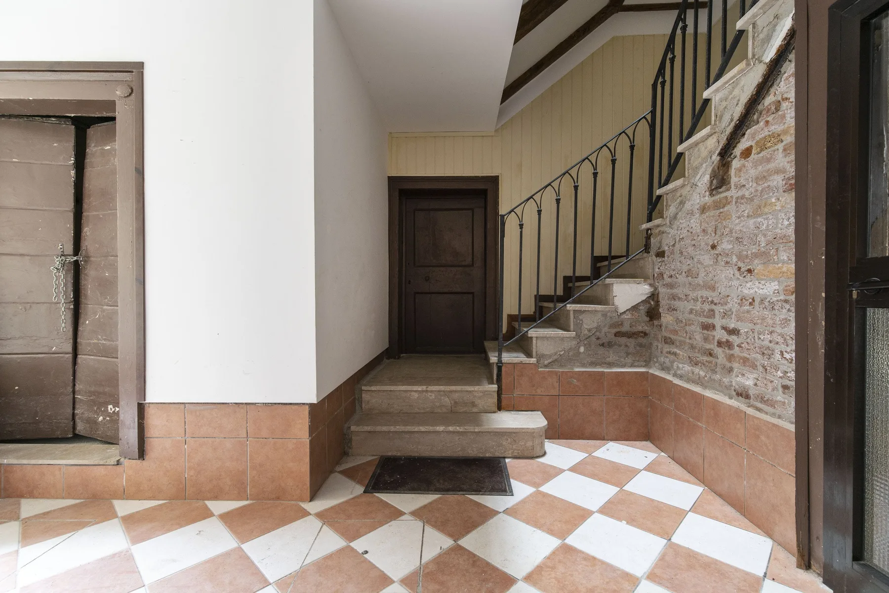 Un recibidor interior con suelo de baldosas y una escalera junto a una pared de ladrillo visto.