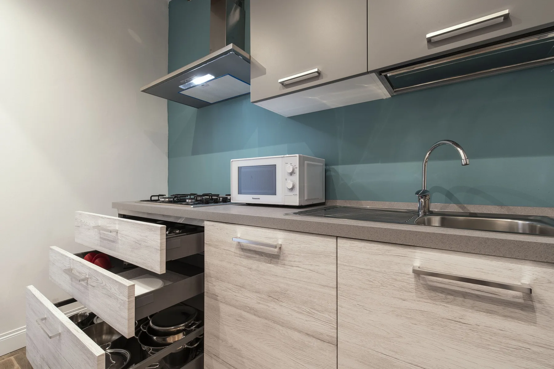 Una cocina moderna con microondas sobre la encimera, fregadero y cajones abiertos.