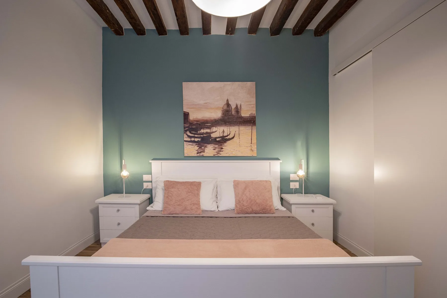 Un dormitorio con una cama centrada frente a una pared de acento verde azulado.