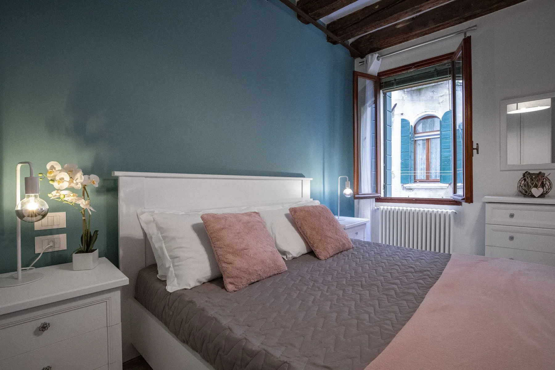 Un dormitorio con una cama tendida y una ventana con vista a un edificio cercano.