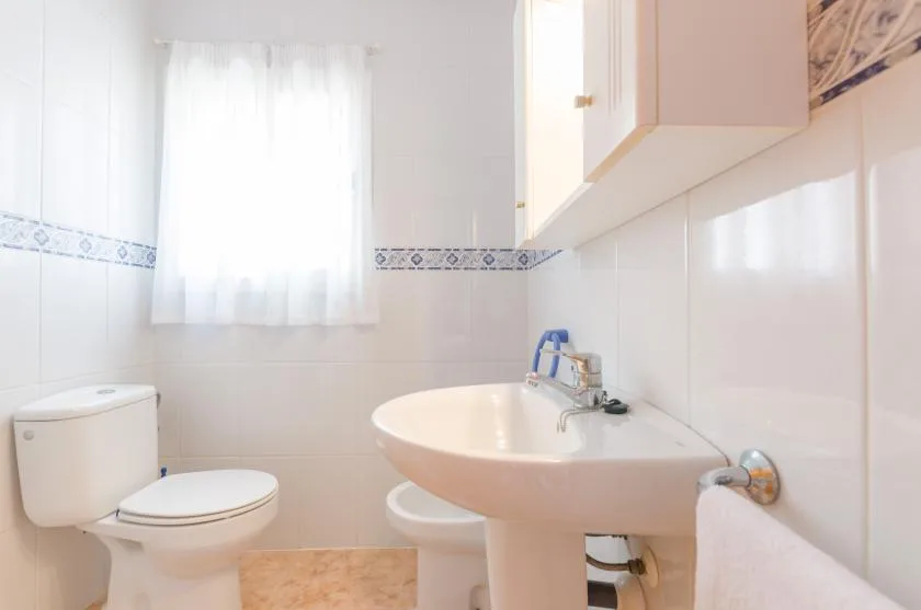 Un baño luminoso con lavabo, inodoro y ventana.