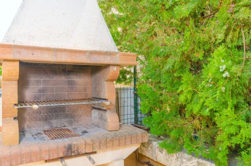 Una barbacoa de ladrillo al aire libre está junto a un follaje verde denso.
