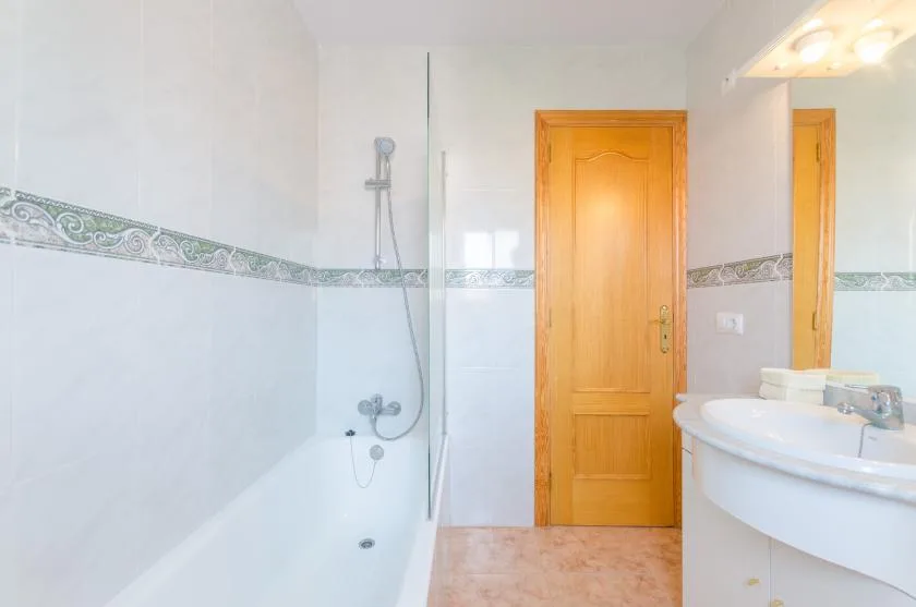 Un baño alicatado con ducha, lavabo y puerta de madera.