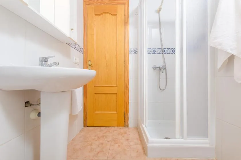 Un baño alicatado con lavabo de pedestal, ducha y puerta de madera.